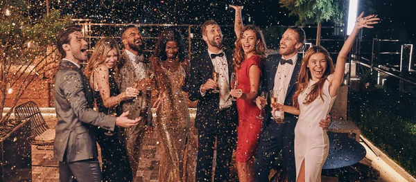 Grupo de personas felices en ropa formal divirtiéndose junto con confeti volando por todos lados — Foto de Stock