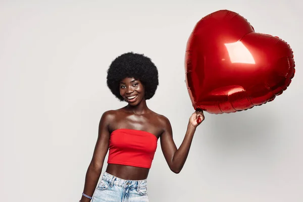 Beautiful young African woman holding red heart shape balloon and smiling — Stock Photo, Image