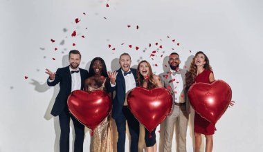 Group of beautiful people in formalwear bonding and holding heart shape baloons