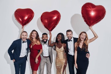 Group of beautiful people in formalwear bonding and holding heart shape baloons