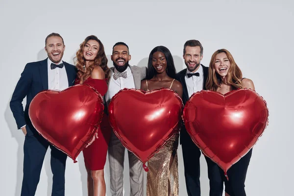Group of beautiful people in formalwear bonding and holding heart shape baloons