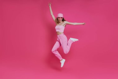 Pembe arka planda atlayan modaya uygun giyinmiş mutlu genç bir kadın.