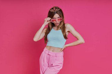 Pembe arka planda duran, funky Crown 'lı oyuncu genç kadın.