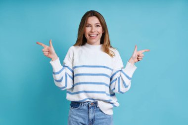 Güzel genç bir kadın mavi arka planda dururken gülümsüyor.