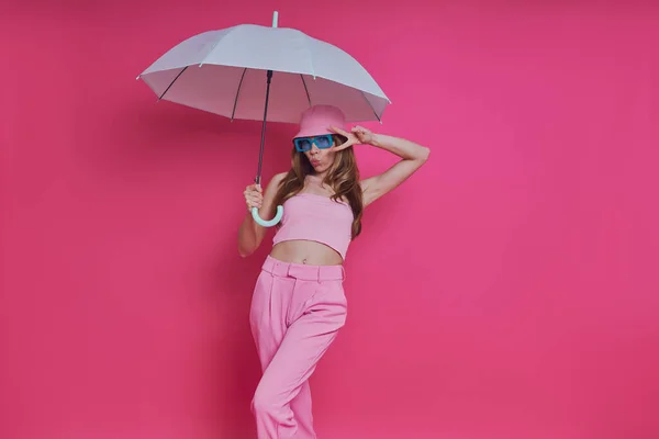 Zabawna Młoda Kobieta Modnej Odzieży Trzyma Parasol Stojąc Różowym Tle — Zdjęcie stockowe