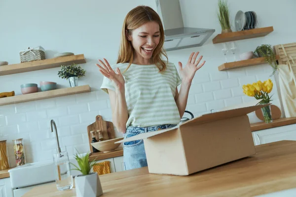 Ενθουσιασμένη Νεαρή Γυναίκα Ξεπακετάρει Κουτί Ενώ Στέκεται Στην Οικιακή Κουζίνα — Φωτογραφία Αρχείου