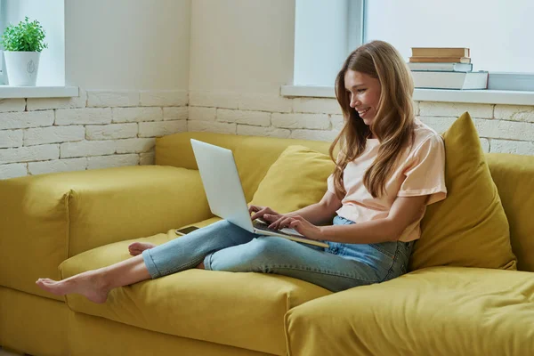 Приваблива Молода Жінка Працює Ноутбуці Посміхається Сидячи Дивані Вдома — стокове фото