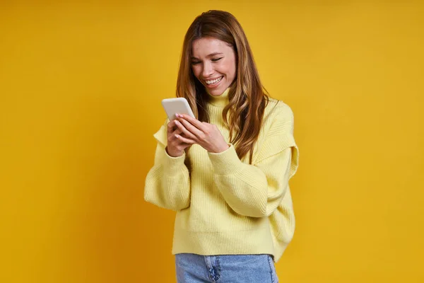 Счастливая Молодая Женщина Используя Свой Смартфон Стоя Желтом Фоне — стоковое фото
