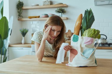Depresyondaki genç bir kadın evdeki mutfakta makbuzları kontrol ediyor.