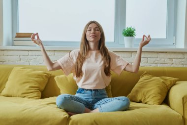 Evdeki kanepede oturmuş meditasyon yapan güzel bir genç kadın.