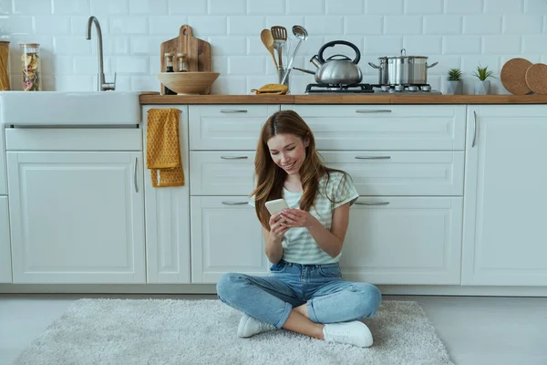 Mulher Bonita Usando Telefone Celular Enquanto Sentado Chão Cozinha — Fotografia de Stock