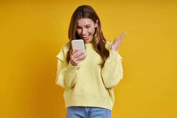 Izgalmas Fiatal Használja Okos Telefon Miközben Áll Szemben Sárga Háttér — Stock Fotó