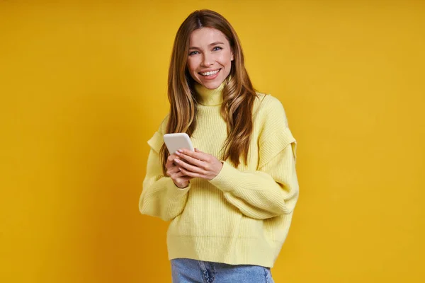 Happy Young Woman Holding Smart Phone While Standing Yellow Background — Stock Photo, Image