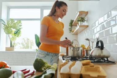 Çekici genç bir kadın ev mutfağında yemek pişiriyor.