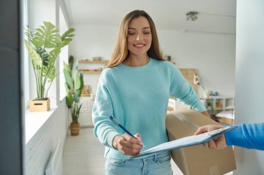 Teslimatçıdan gelen kutuyu kabul eden ve kağıt imzalayan mutlu genç kadın.