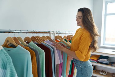 Moda mağazasında kıyafet seçen mutlu genç bir kadın.