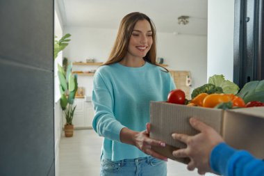 Güzel genç bir kadın, evdeki teslimatçıdan gelen yiyeceklerle dolu kutuyu kabul ediyor.