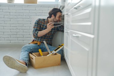 Genç adam ev mutfağında lavabo tamir etmekle meşgul.
