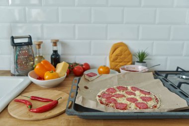 Mutfak tezgahında duran ev yapımı pizza ve malzemeler.