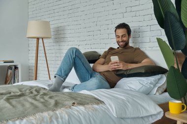 Evde dinlenirken cep telefonu kullanan yakışıklı genç adam.