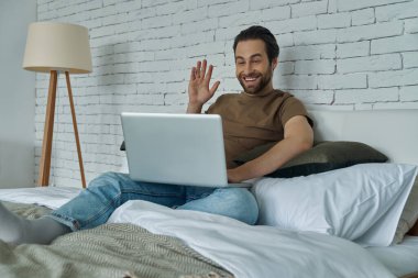 Evde dizüstü bilgisayar kullanırken video görüşmesi yapan yakışıklı genç adam.