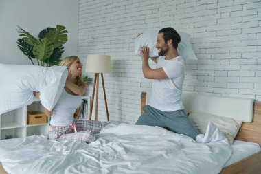 Evdeki yatakta yastık savaşı yapan neşeli genç çift.