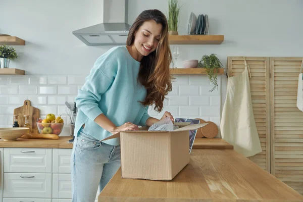 Bella Giovane Donna Disimballaggio Scatola Mentre Piedi Presso Cucina Domestica — Foto Stock