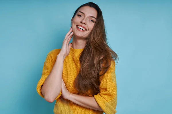 Mulher Bonita Tocando Rosto Sorrindo Enquanto Estava Contra Fundo Azul — Fotografia de Stock