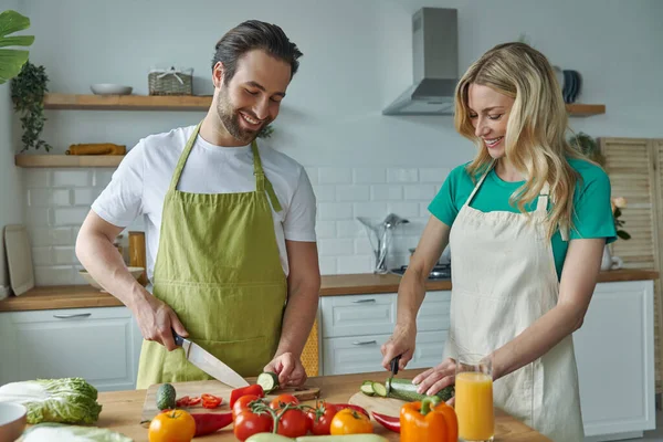 一对快乐的年轻夫妇在厨房切蔬菜 — 图库照片