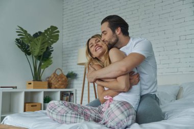 Mutlu genç çift yatakta eğlenirken sarılıp öpüşüyor.