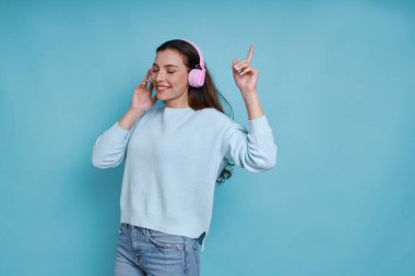 Kulaklıklı çekici bir kadın mavi arka planda dururken müzik dinliyor.