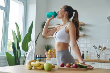 Spor elbiseli güzel bir kadın mutfakta dururken protein kokteyli içiyor.
