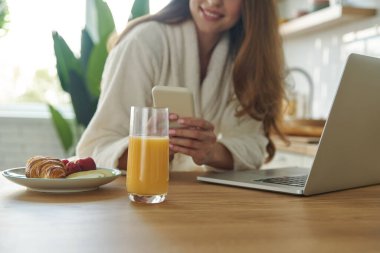 Bornozlu güzel bir kadının mutfakta vakit geçirirken teknolojilerini kullanması.