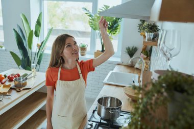 Kendine güvenen genç bir kadının yemek kapüşonunu takıp ev mutfağında durmasının en iyi görüntüsü.