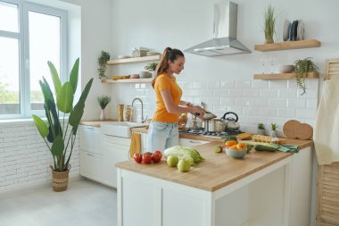 Modern mutfakta yemek pişiren kendinden emin genç bir kadın.