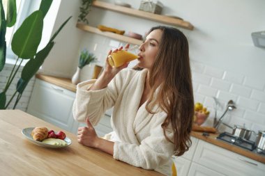 Modern mutfakta kahvaltı eden bornozlu çekici genç bir kadın.