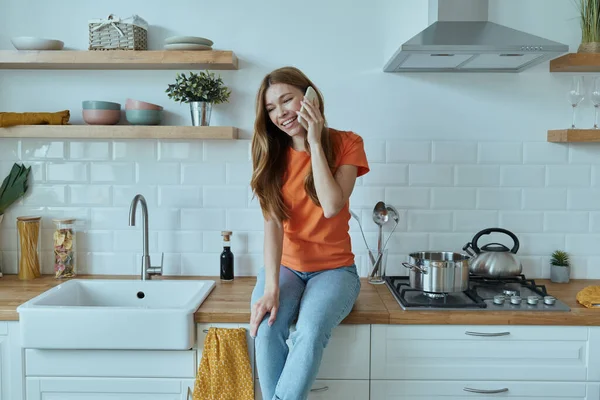 Güzel genç bayan mutfak tezgahında otururken akıllı telefon kullanıyor.