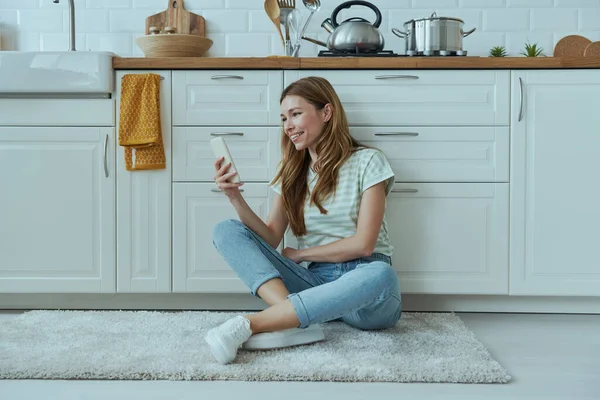 Молодая Женщина Пользуется Мобильным Телефоном Сидя Полу Кухне — стоковое фото