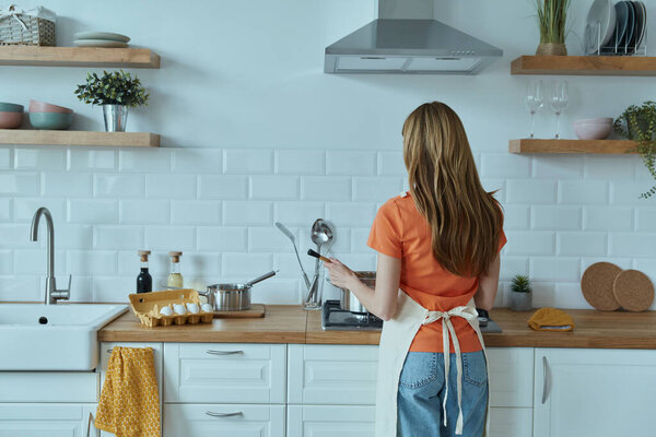 Взгляд сзади на молодую женщину, готовую на домашней кухне