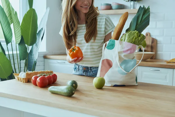 Genç bir kadının evdeki mutfakta dururken sağlıklı yiyeceklerle bavulunu boşaltması.