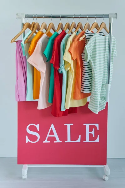 Colorful clothes hanging on clothes rack with sale banner