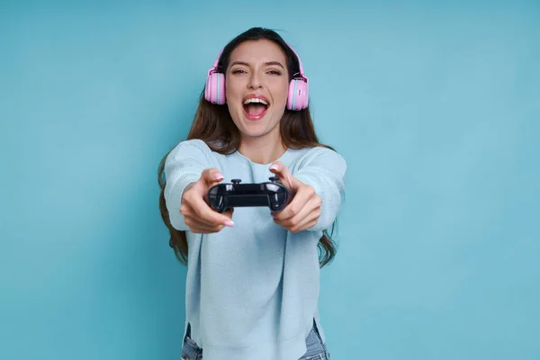 Hravá Žena Sluchátkách Drží Joystick Usmívá Zatímco Stojí Modrém Pozadí — Stock fotografie
