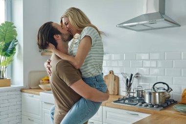 Güzel, genç bir çift. Evcil mutfakta dururken sarılıp öpüşüyorlar.