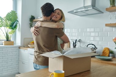 Genç çift mutfak tezgahında açık kutu yatarken kucaklaşıp gülümsüyor.