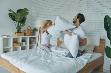 Evdeki yatakta yastık savaşı yapan neşeli genç çift.