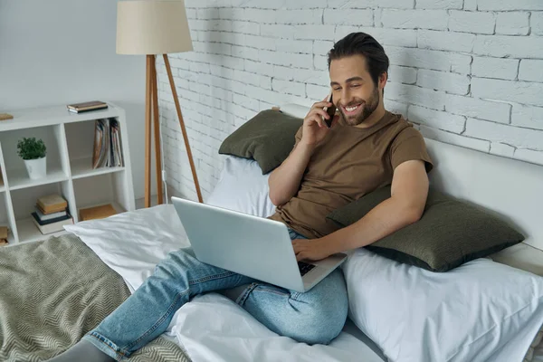 Fešák Mladý Muž Pomocí Notebooku Mluvit Mobilním Telefonu Při Relaxaci — Stock fotografie