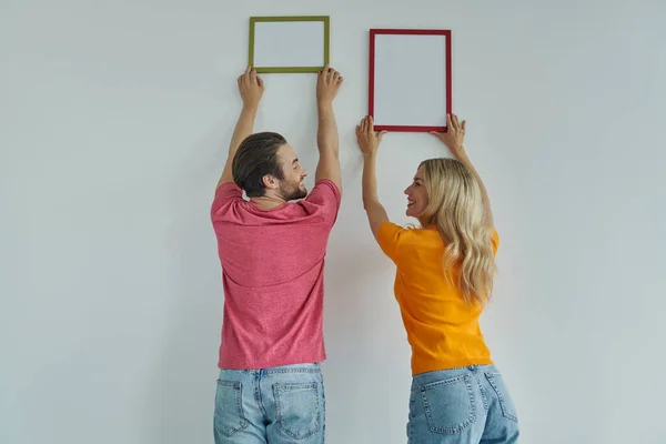 Rear View Beautiful Young Couple Hanging Picture Frames Wall Smiling — Stock Photo, Image