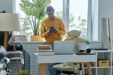 Ofiste çalışırken akıllı telefon kullanan yakışıklı, melez bir ırk adamı.