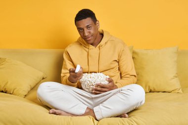Sıkıcı adam televizyon seyrediyor ve sarı arka planda kanepede dinlenirken atıştırmalık yiyor.