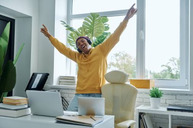 Neşeli melez, kulaklıklı bir ırk adamı iş yerinde dikilirken el kol hareketi yapıyor.